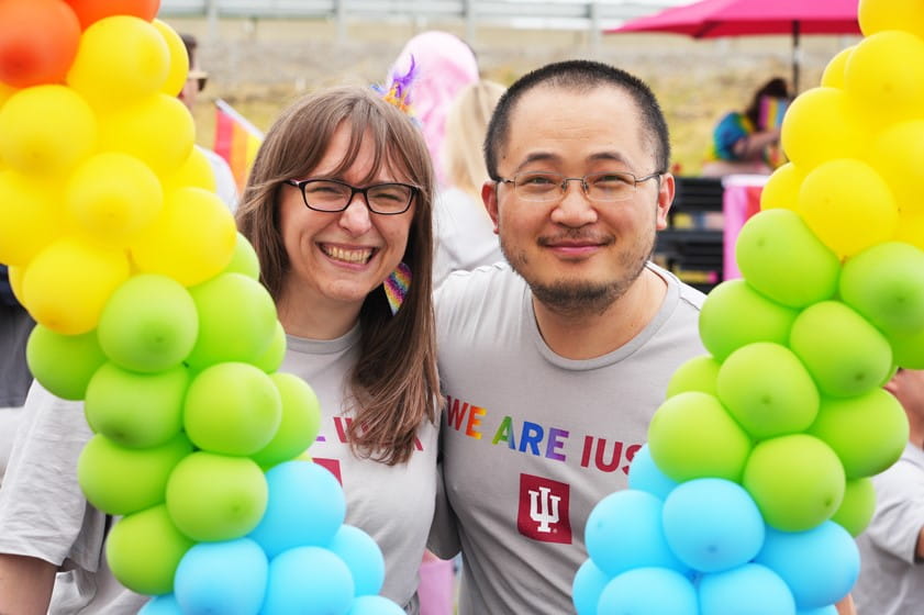 two iu staff members smile in between a balloon arch at the pride parade in indy