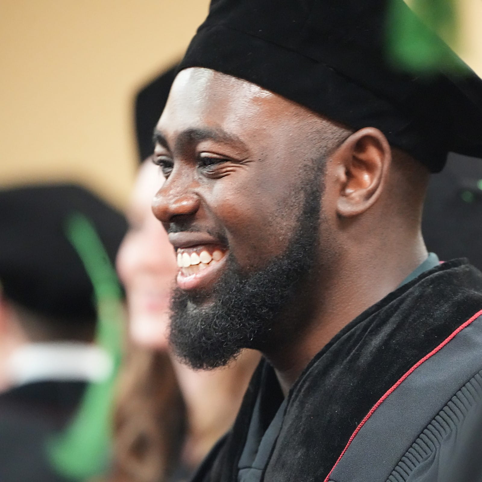 a student in graduation hat and gown smiles during the ceremony