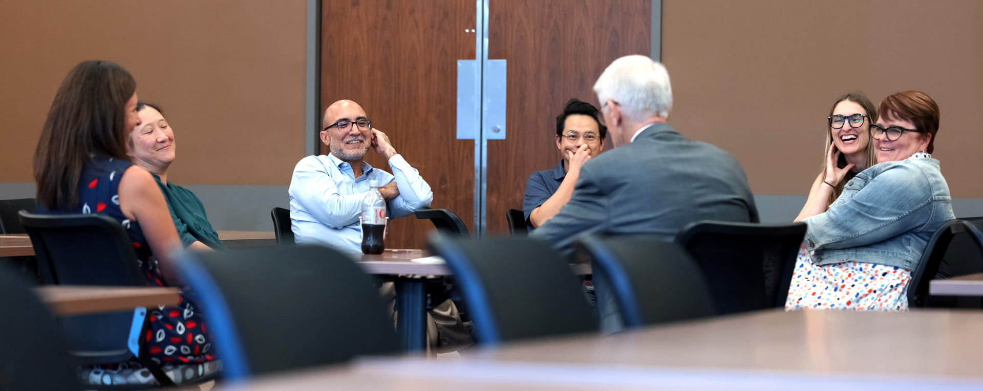 a diverse group of faculty sit around a table speaking with a guest lecturer