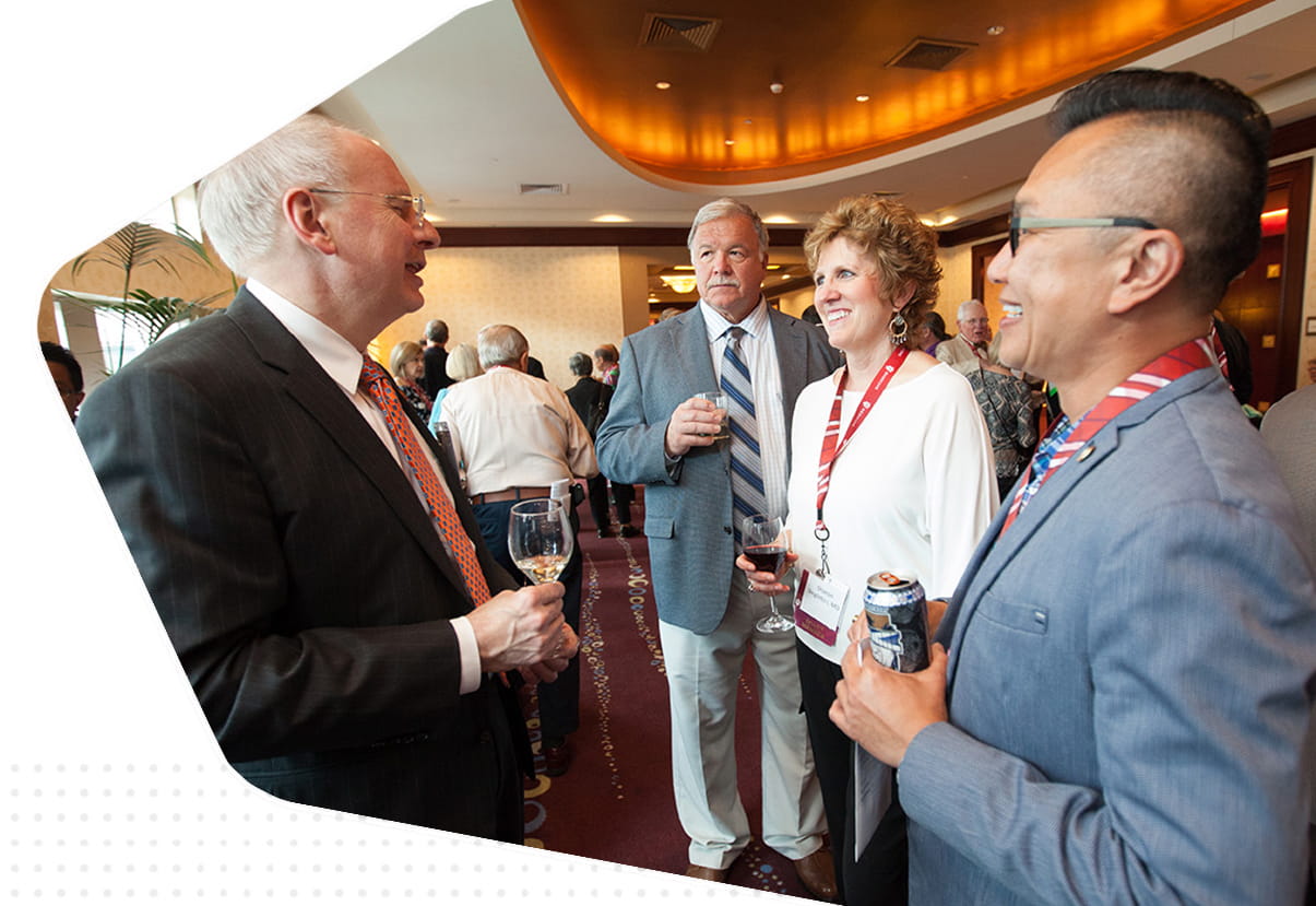 a group of alumni laugh and talk holding drinks