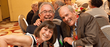 three alumni lean in together and smile at a celebration dinner