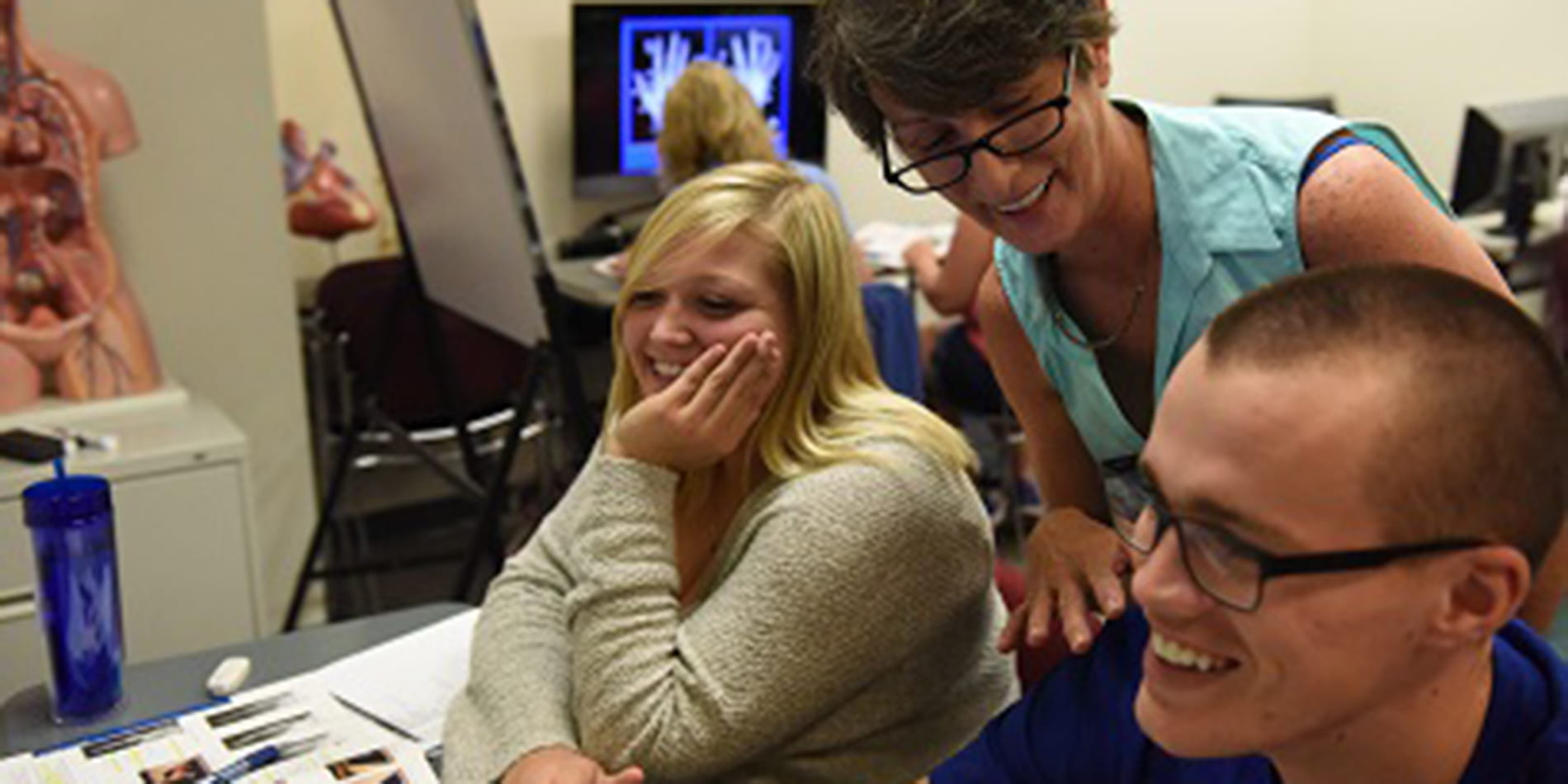Students smiling looking at screen, faculty member behind them smiling