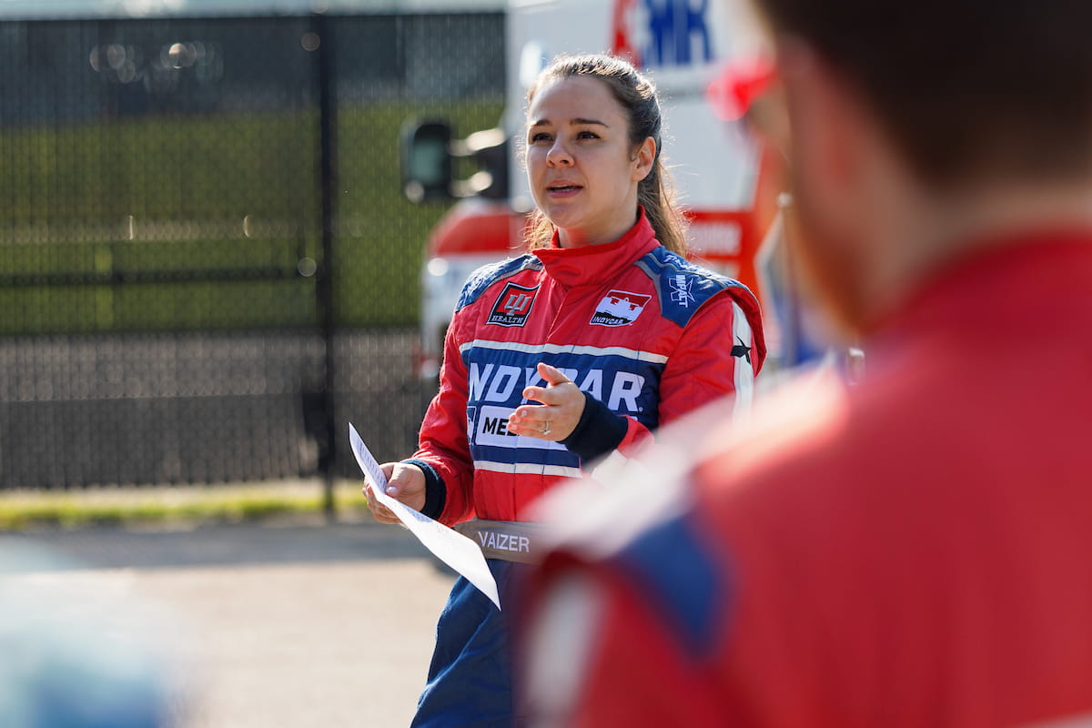 Julia Vaizer, dressed in her IndyCar Medical Team fire suit, holds a paper while she gives a safety briefing