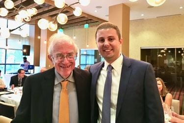 Larry Einhorn and Nabil Adra pose together, both wearing suits and ties, inside a restaurant