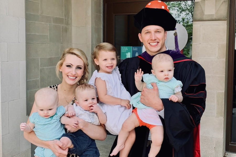Chelsea and Cameron Fathauer, dressed in cap and gown for his law school graduation, holding their four small children