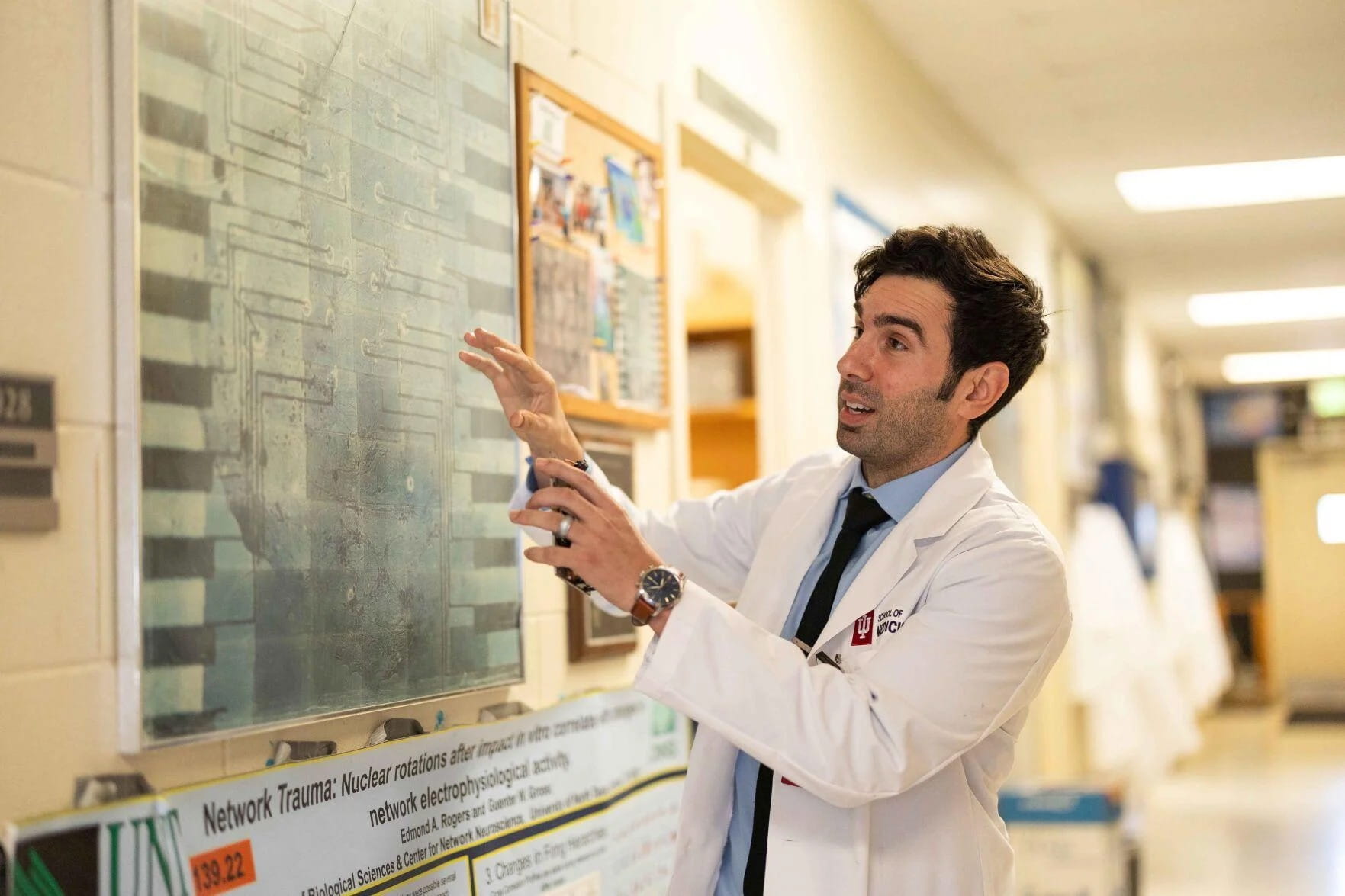 Ed Rogers explains the multi-network structure of TBI-on-a-chip design using a diagram in a hallway at Purdue.