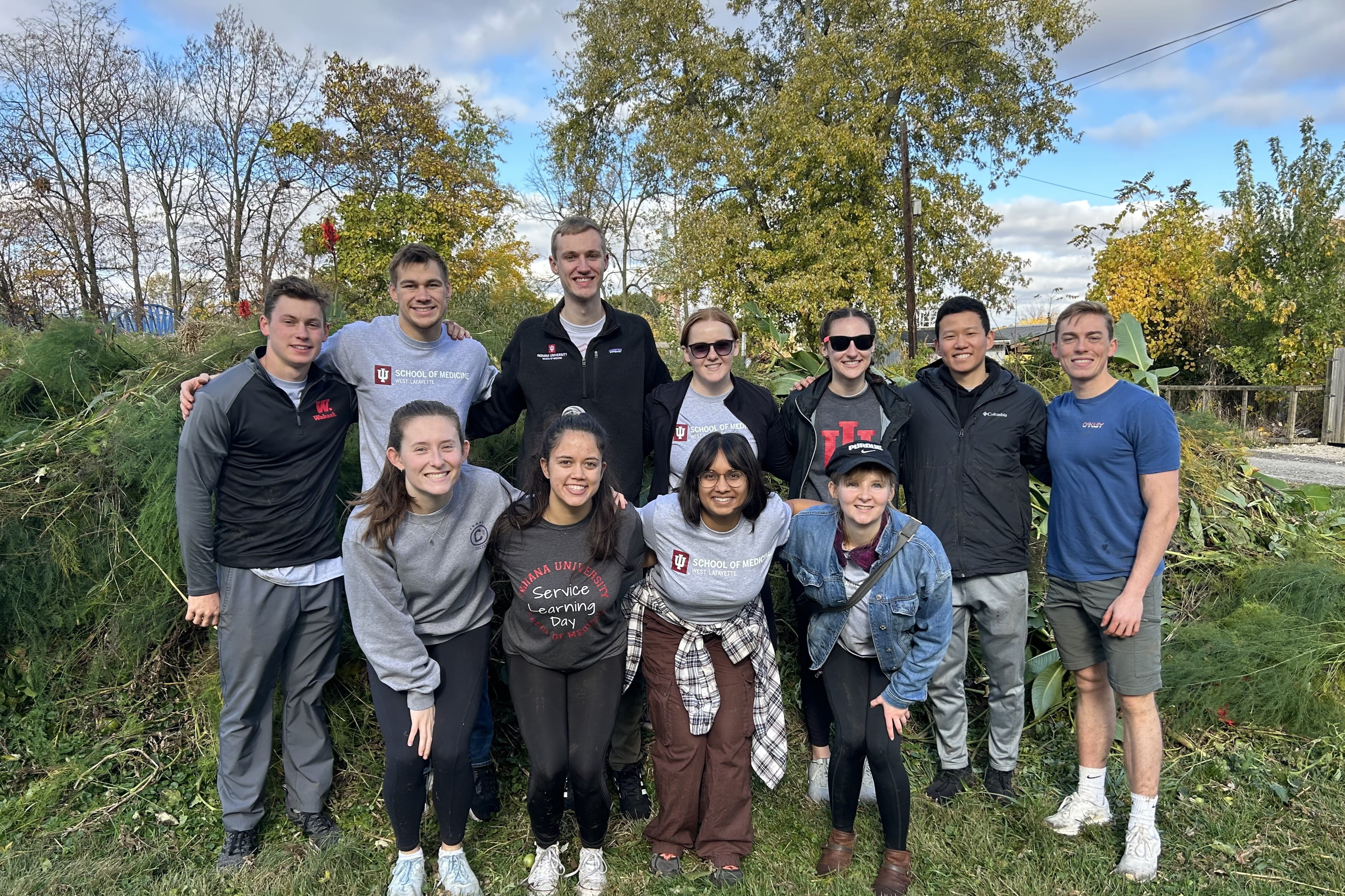 a group of MD students in west lafayette pose in front of a large pile of weeds at a community garden