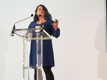Hannah Kline in blue dress at podium, presenting research at the International Behavioral Neuroscience Symposium in Scotland in 2022.