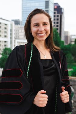 Juliet Hardesty (caucasian female with brown hair) wearing her graduation gown with the Indianapolis skyline behind her
