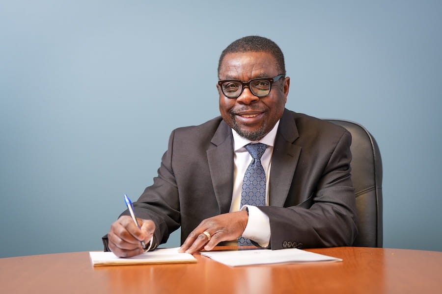 Kola Okuyemi sits at a desk with pen in hand