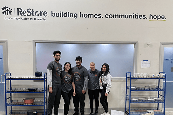 Five IU med students pose in front of a Habitat ReStore sign.