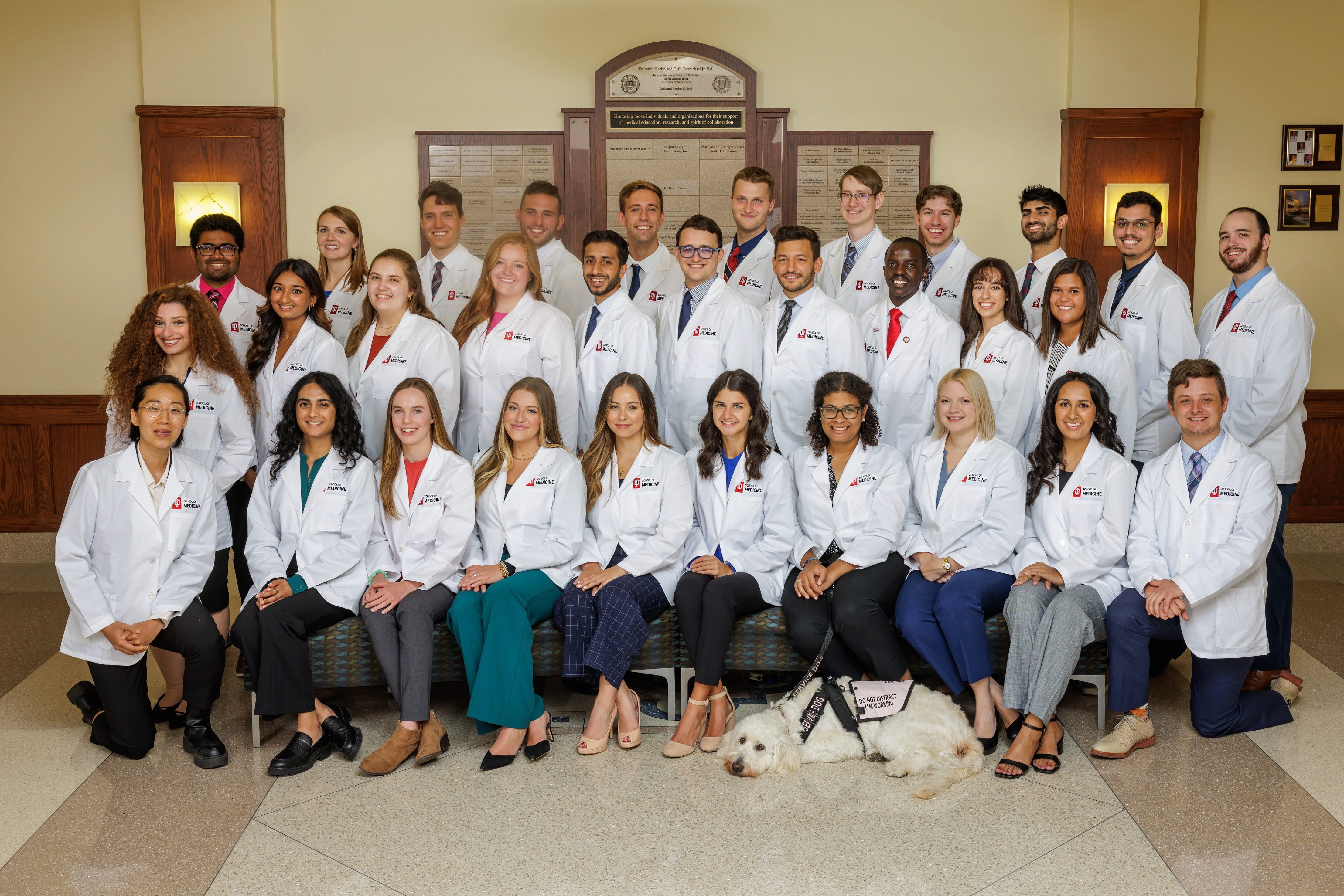 The IU School of Medicine--South Bend Class of 2027 pose in white coats for a class portrait including Kennedy Onuoha's service dog Aura.