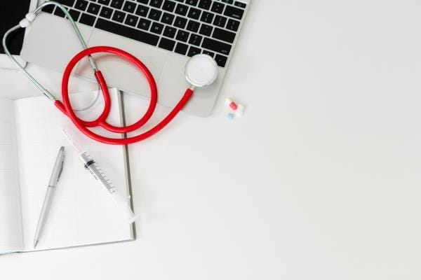 a red stethoscope lays across an open laptop computer