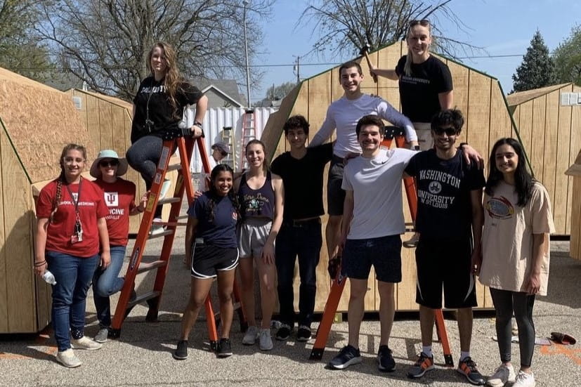 a large group of students stand in front of sheds they are painting with Habitat for Humanity