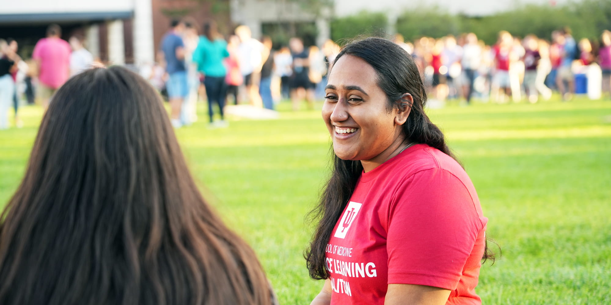 two students sit on the grass on a sunny day outside on the IU Indianapolis campus