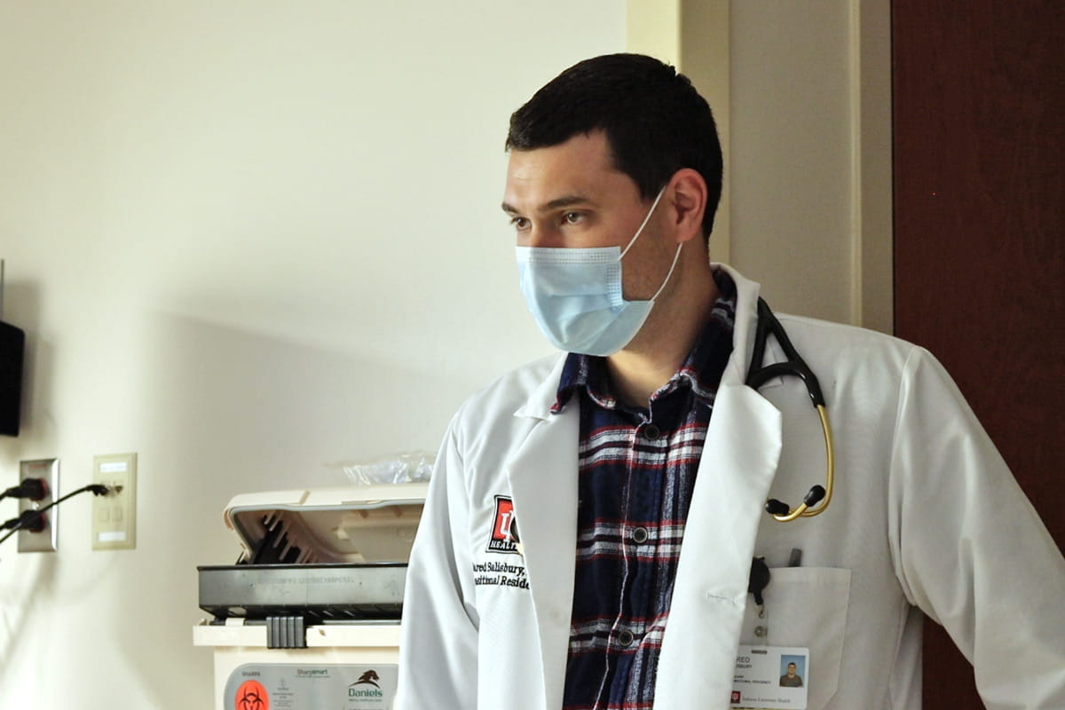 resident wearing a mask and white coat talks to a patient not seen in the photo