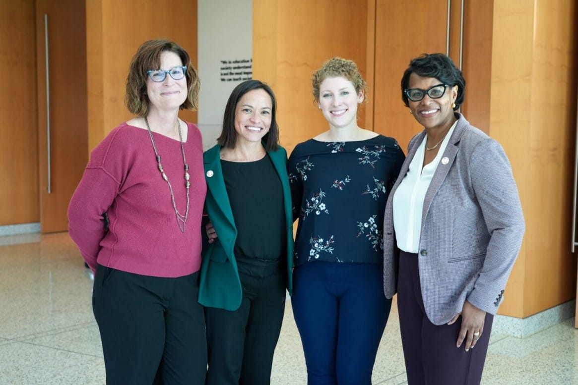 four women standing with their arms around each other
