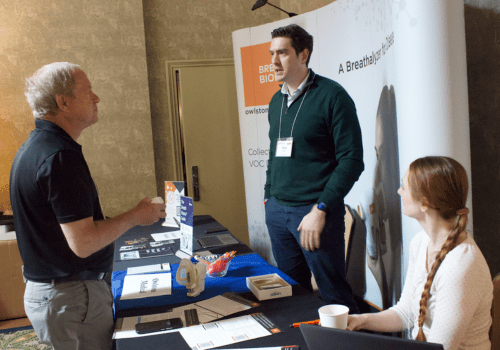 Breath Summit 2024 sponsor table hosts chatting with an attendee