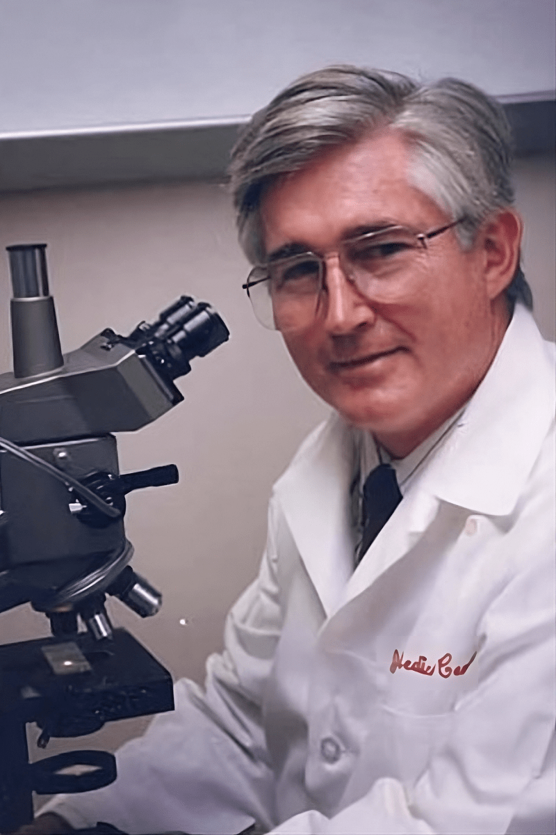 Evan Farmer sits at a microscope wearing a lab coat