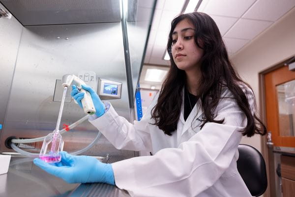 A female-presenting scientist works in a lab. She is using equipment to transfer liquid to a bottle.
