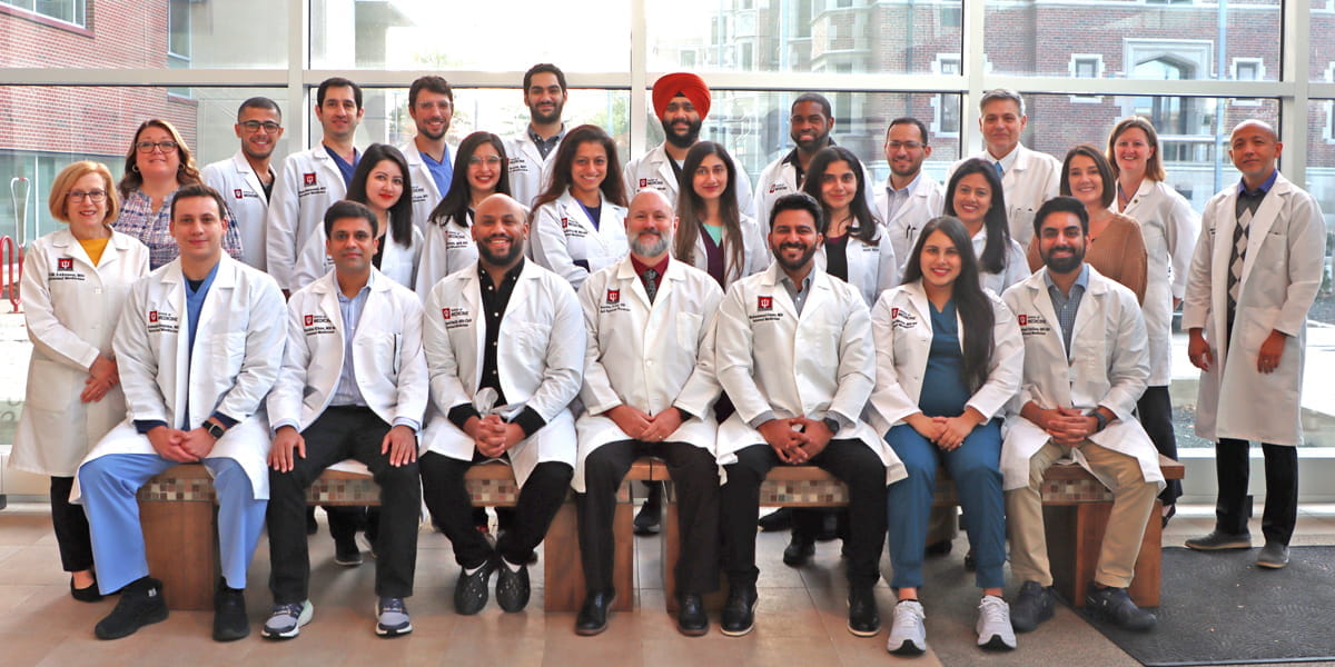 three rows of physicians in white coats sit and stand for a class photo