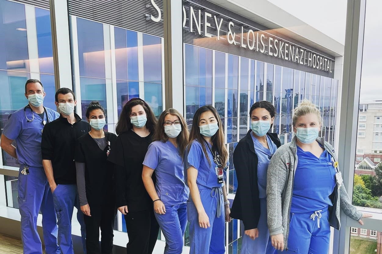 Residents wearing masks and scrubs pose for a photo in front of Eskenazi hospital