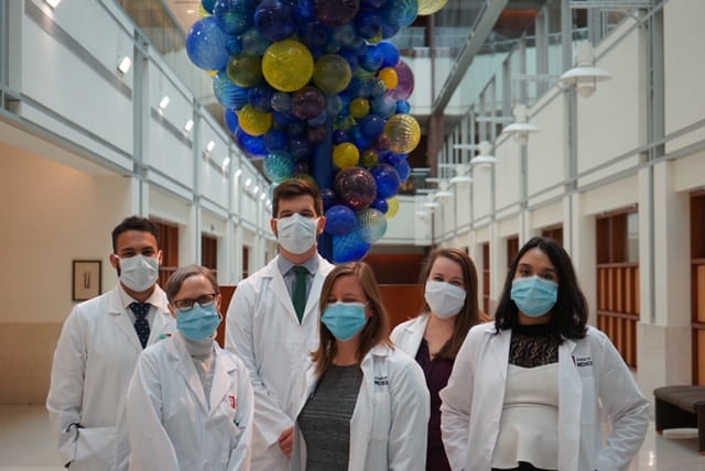 Six fellows in masks and white coats stand together for a group photo