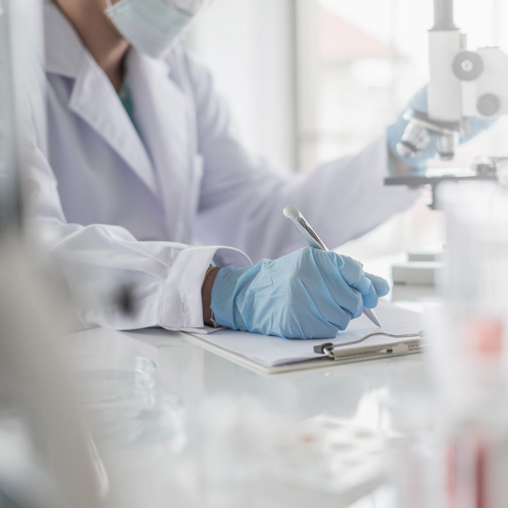 a fellowship student at work in the lab wearing a white lab coat, gloves and mask