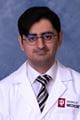 Obaid wearing a lab coat and tie with short dark hair and glasses