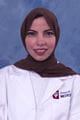 Reem wears a lab coat and brown head scarf