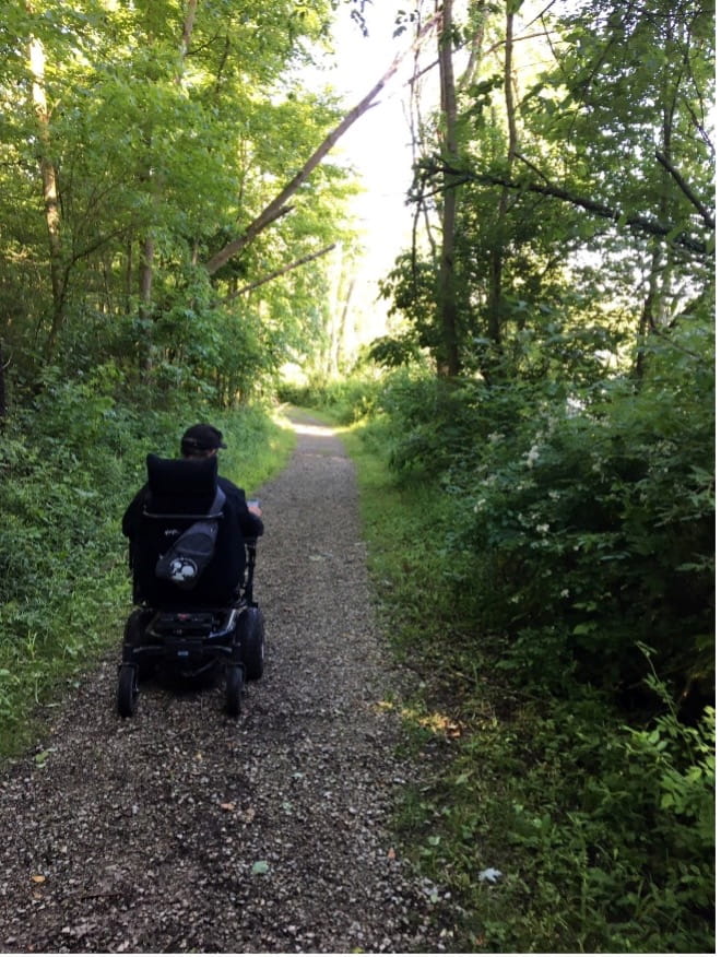 An individual in a wheelchair moves along a wooded path.