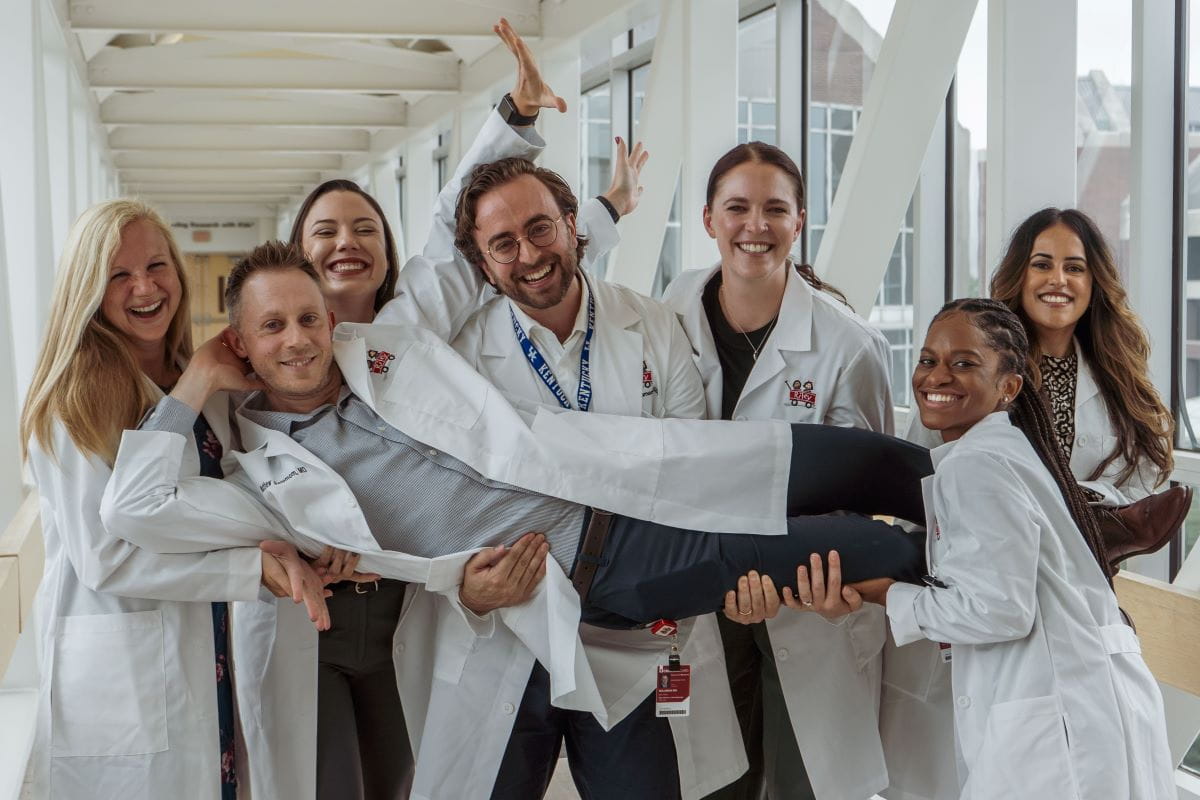six fellows in white coats hold up a seventh fellow in a funny group photo