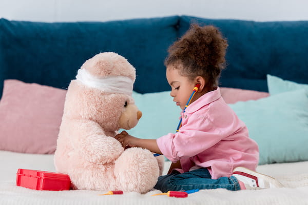 A young child plays pretend doctor with a stuffed bear.