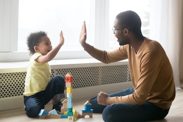 A father and daughter high five while playing with blocks.