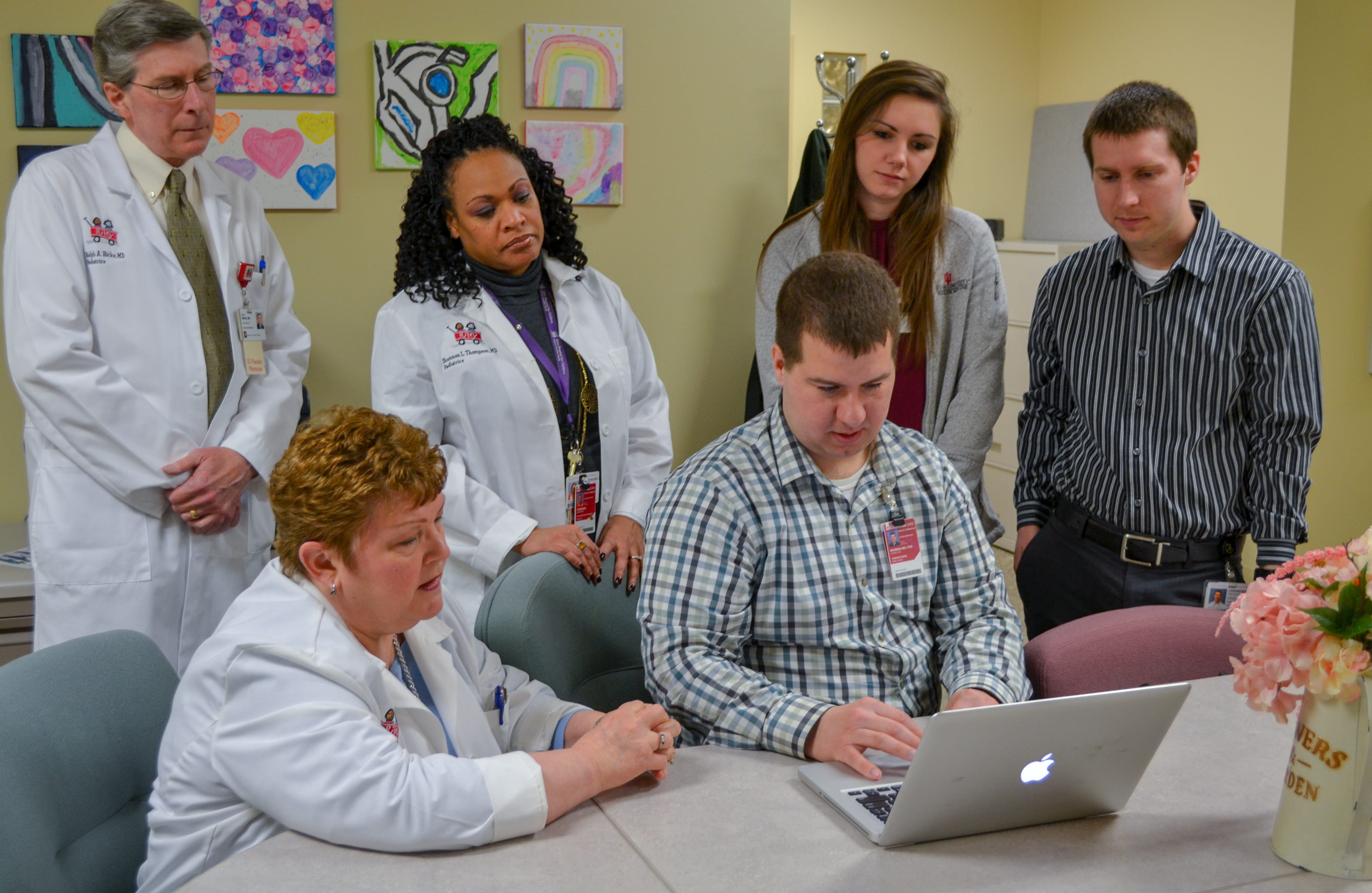 faculty and fellows gather around a computer together to discuss a case