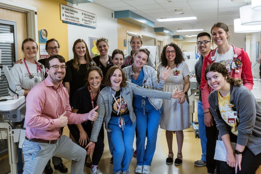 a group of pediatric hem-onc fellows stand grouped in the hall of the hospital with smiles and thumbs up