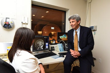 Two researchers talking, one sitting in chair and the other leaning on table 