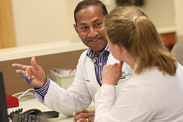 Two physicians sitting at desk facing one another and talking.
