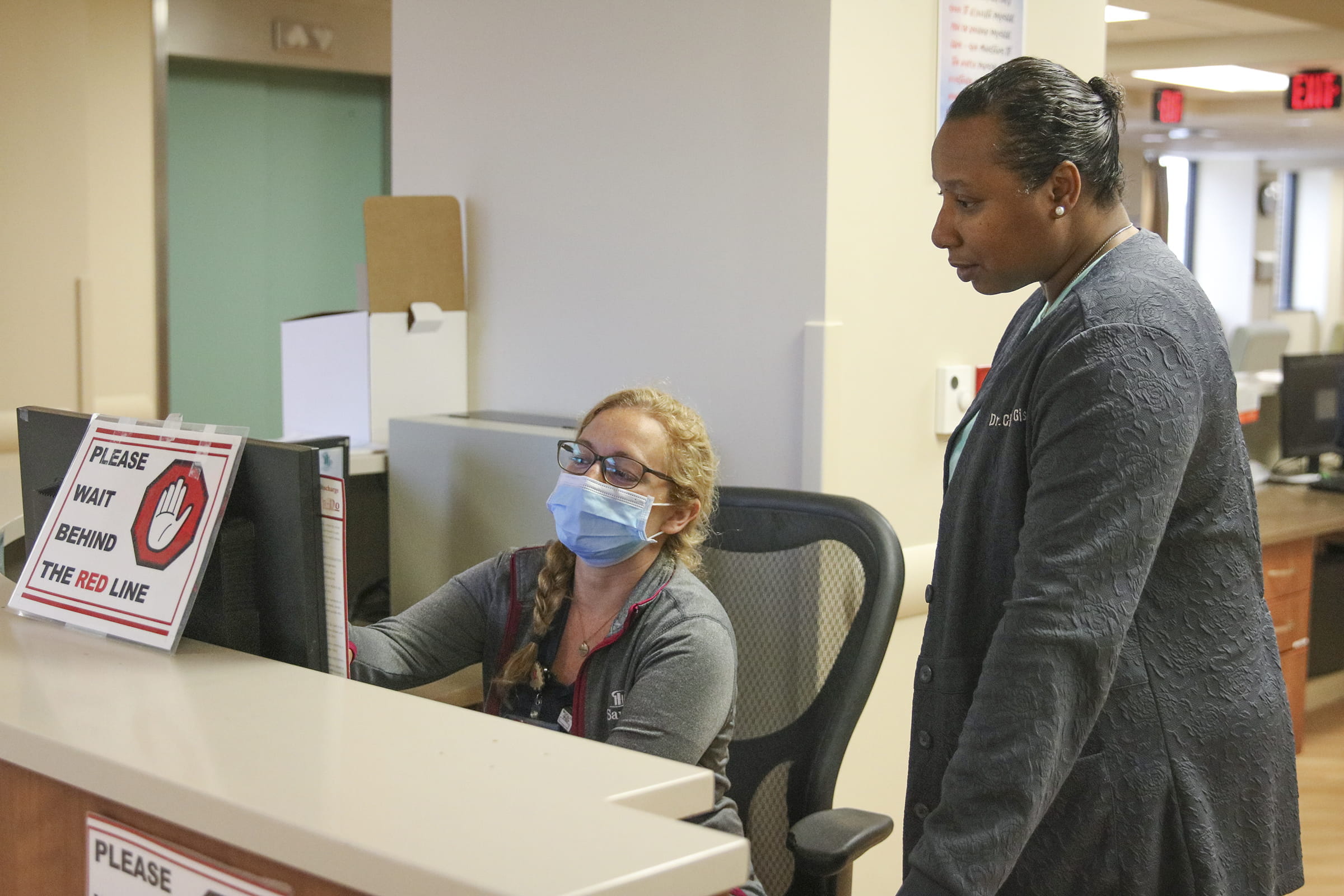 Doctors in masks and scrubs talking by administrative counter in hospital