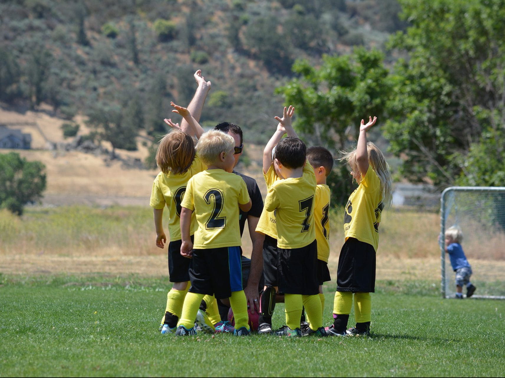 a group of small children in soccer uniforms huddle together on the field