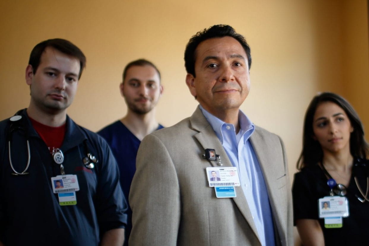a faculty member stands in front of a group of medical students looking confidently at the camera
