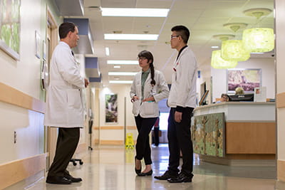 A physician talks with medical students in a hospital hallway