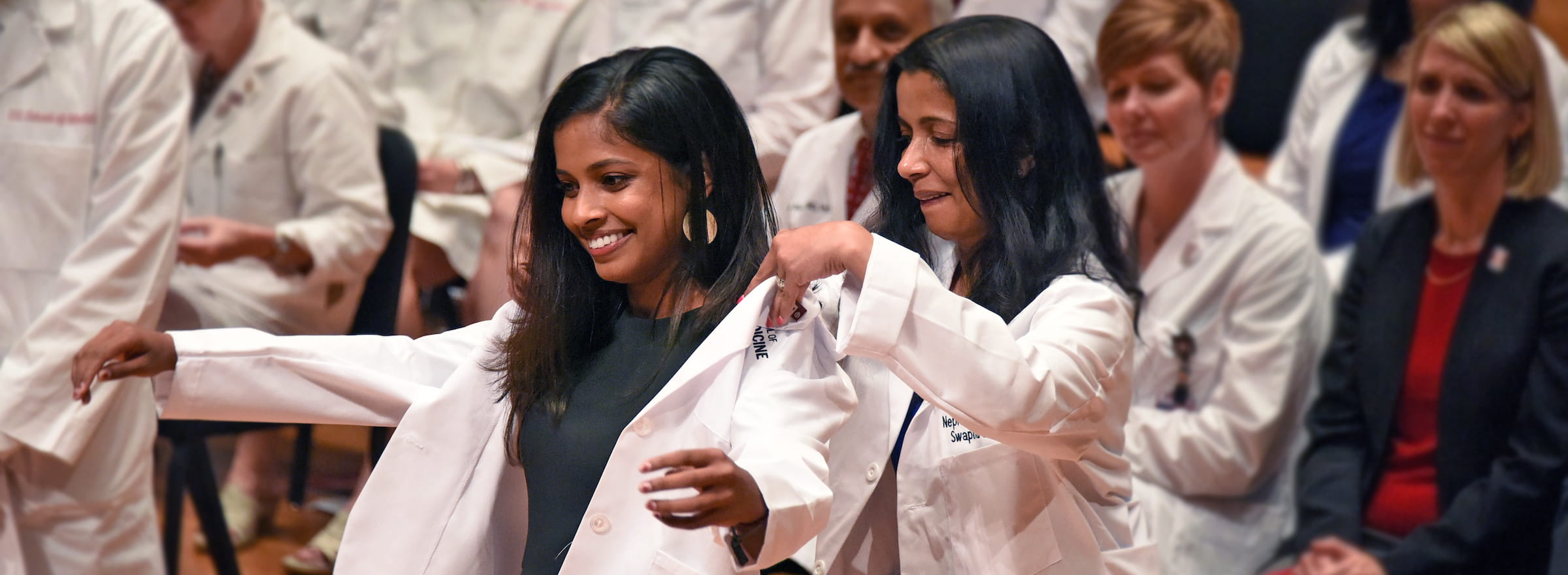 during the white coat ceremony, a mother slides a new white coat over her daughters shoulders
