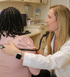 Jessica Parker, MD, listens to a patient's heart with her stethoscope on the patient's back