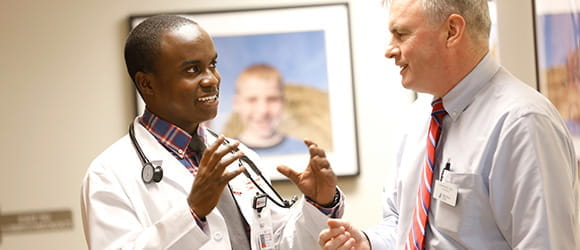 a black medical student with a smile on his face speaks to a faculty member