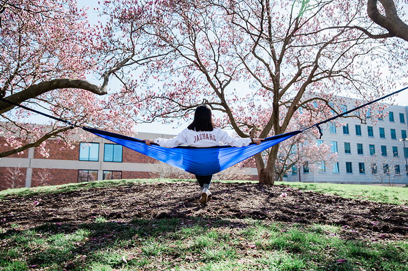 A woman in a Jaguars sweatshirt relaxes in a hammock on campus