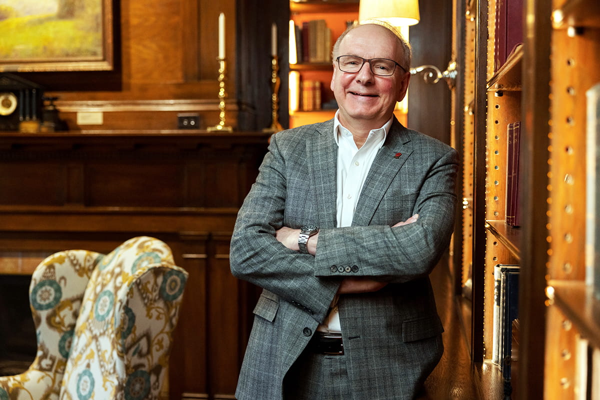 dean hess stands with his arms folder leaning against a shelf in his home library