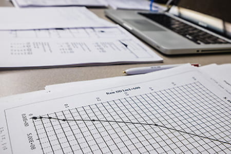 a paper with a graph on it sits in the foreground with a laptop in the background